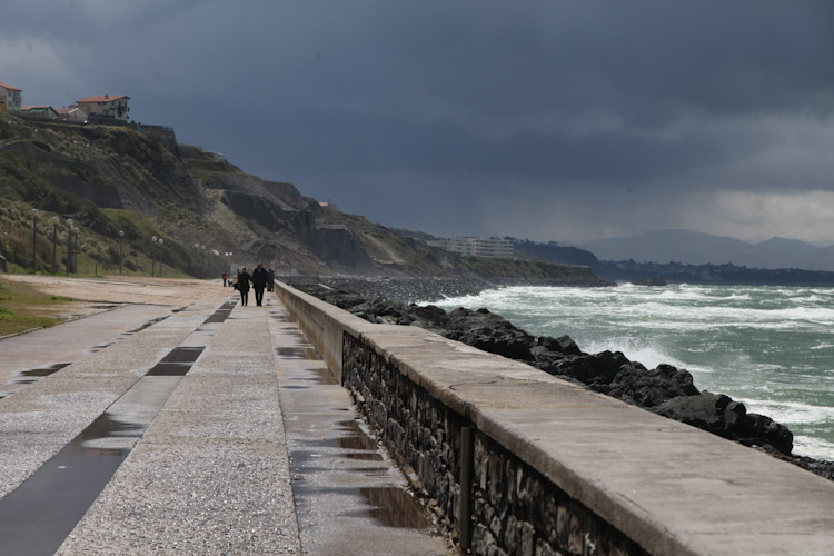 Couple strolls the sea as the clouds briefly part in Biarritz, France.